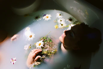woman sitting in bathtub with white and yellow daisy flowers