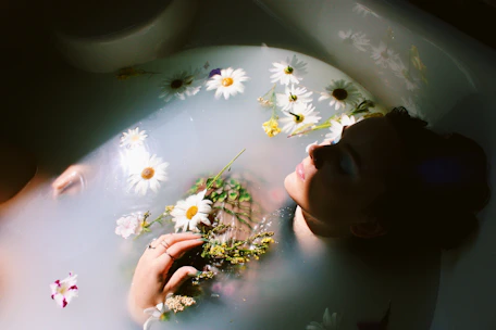woman sitting in bathtub with white and yellow daisy flowers