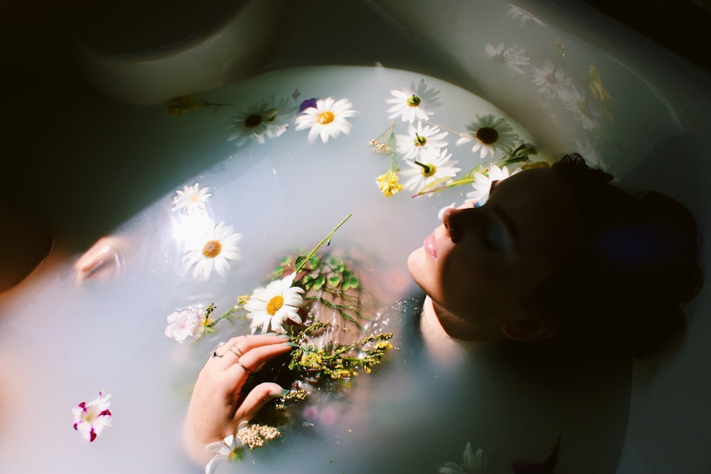 Donna che si siede nella vasca da bagno con i fiori bianchi e gialli della margherita