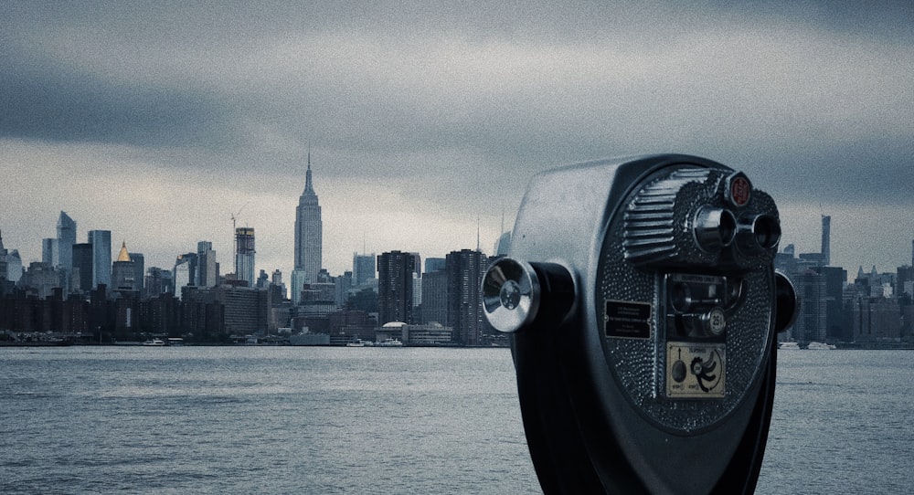 black and gray coin-operated telescope viewing sea and New York City under white and gray sky during daytime