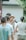 A group of people gather outdoors for a photography session. A woman in a straw hat holds a camera and focuses on taking a picture. Several people stand around her, casually dressed, and the scene has a relaxed, candid atmosphere.