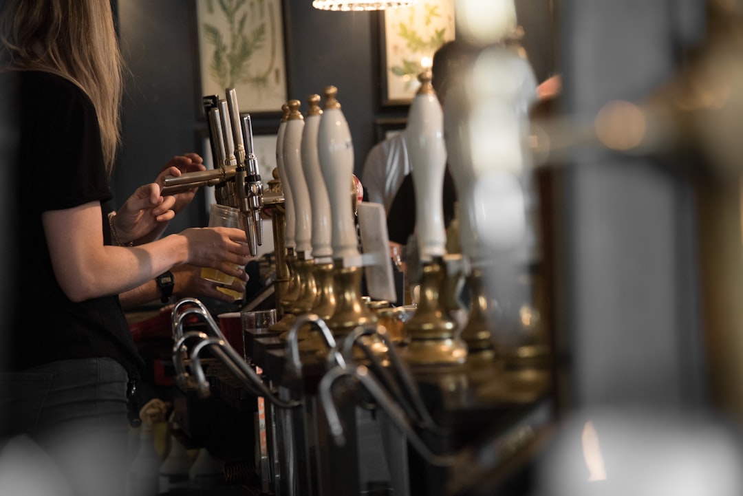 A woman is pouring beer into the glass. She's working at the bar in restaurant which is located in United Kingdom.