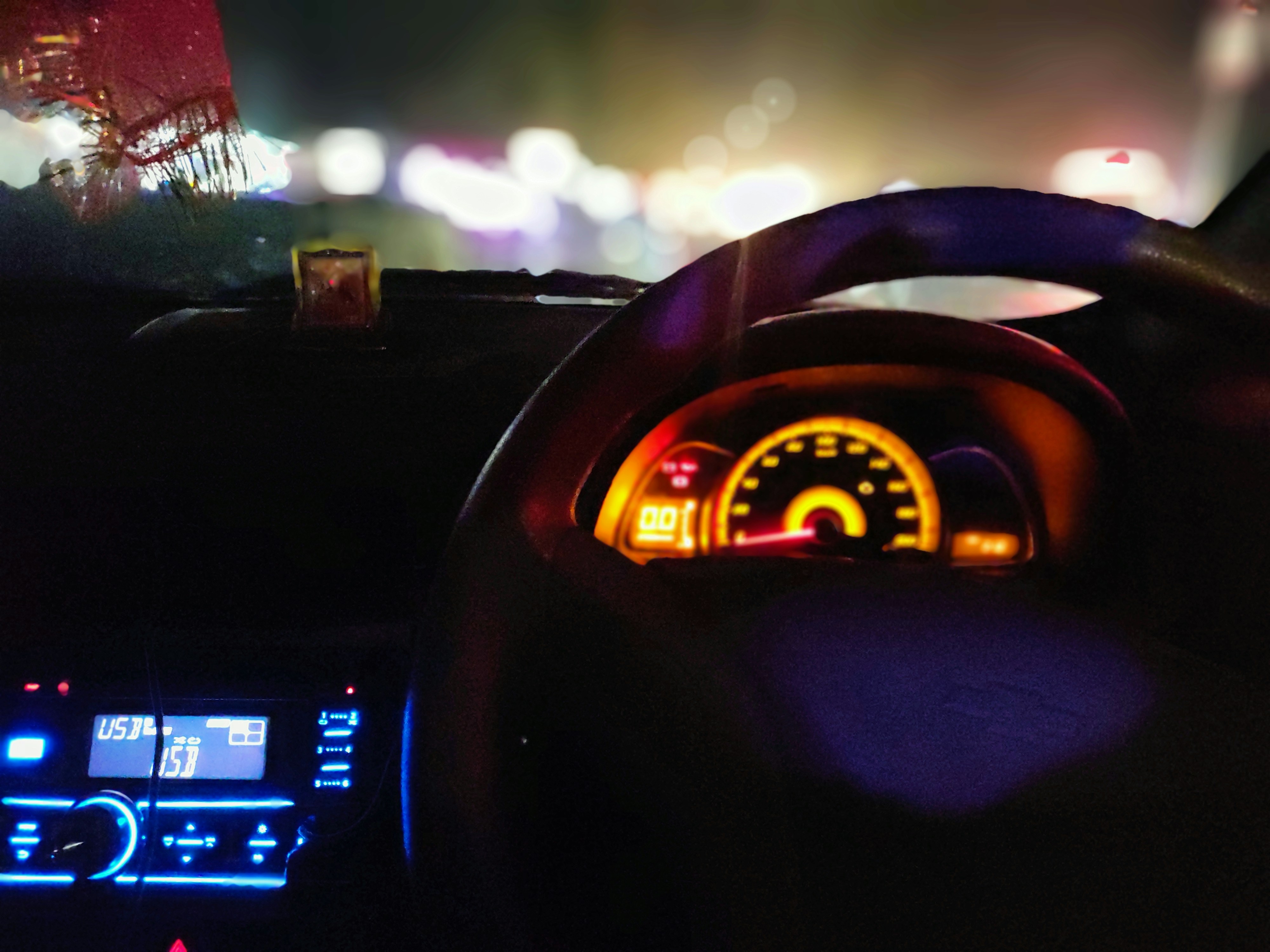 Car interior dashboard at night with warm ambient lighting and stereo system glowing, deep atmospheric shadows