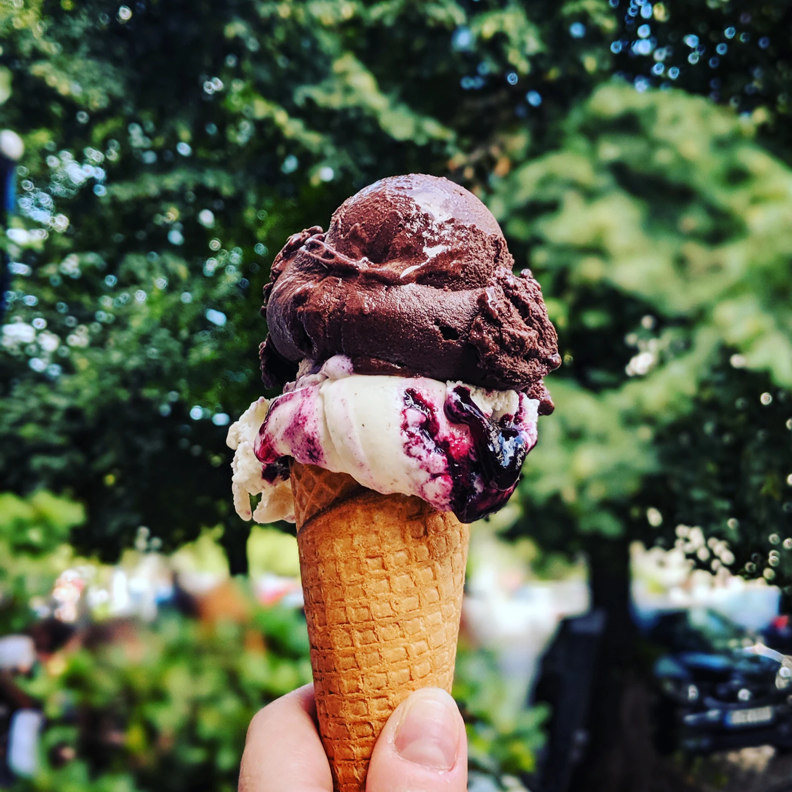 Hand mit einer Waffel mit zwei Kugeln Eis vor sommerlichem Grün