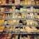 A well-stocked supermarket dairy section featuring a wide variety of cheeses displayed on shelves. The assortment includes round, rectangular, and wedge-shaped packages with labels in multiple languages. Prices are visible on digital screens beneath each item.