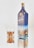 A tall, elegant bottle of whiskey with a blue label next to a glass filled with a brown liquid. The bottle features a gold cap and has branding and logos on its front.