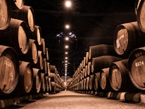 Rows of aging bourbon barrels stacked in a rustic warehouse with soft sunlight filtering through.