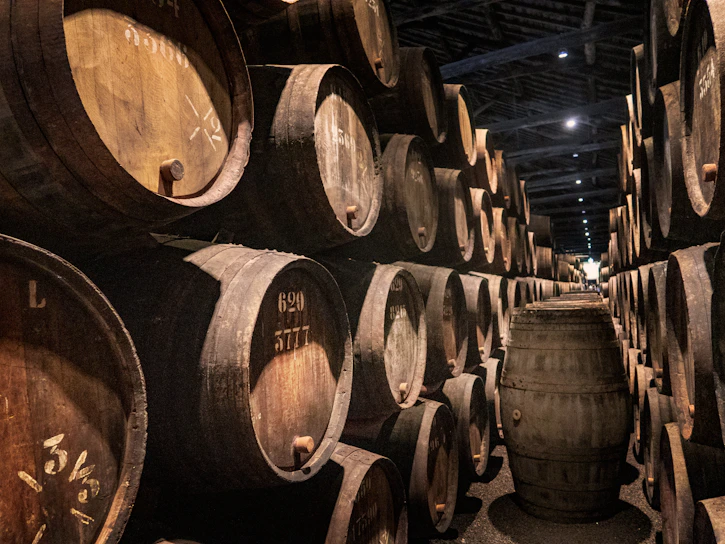 A rustic wooden barrel resting in a dimly lit cellar, surrounded by agave plants.