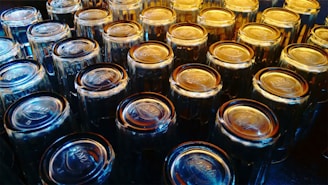 A collection of clear, upside-down drinking glasses arranged in rows on a reflective surface. The glasses are catching light, resulting in a gradient of blue and amber hues, giving them a visually appealing appearance.