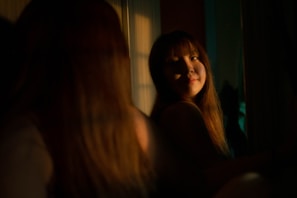 Confident woman with long, lush lashes looking into the mirror with soft golden lighting