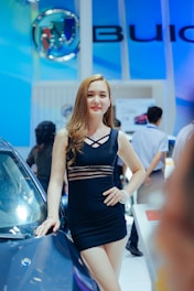 A poised exhibition model elegantly presenting a luxury car at a sleek auto show booth.