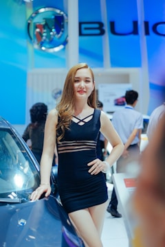 A poised exhibition model elegantly presenting a luxury car at a sleek auto show booth.
