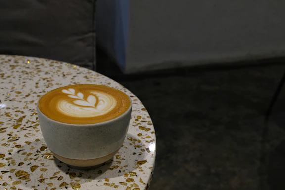 A warm latte in a cream-colored cup on a wooden table with soft blush and terracotta accents around.