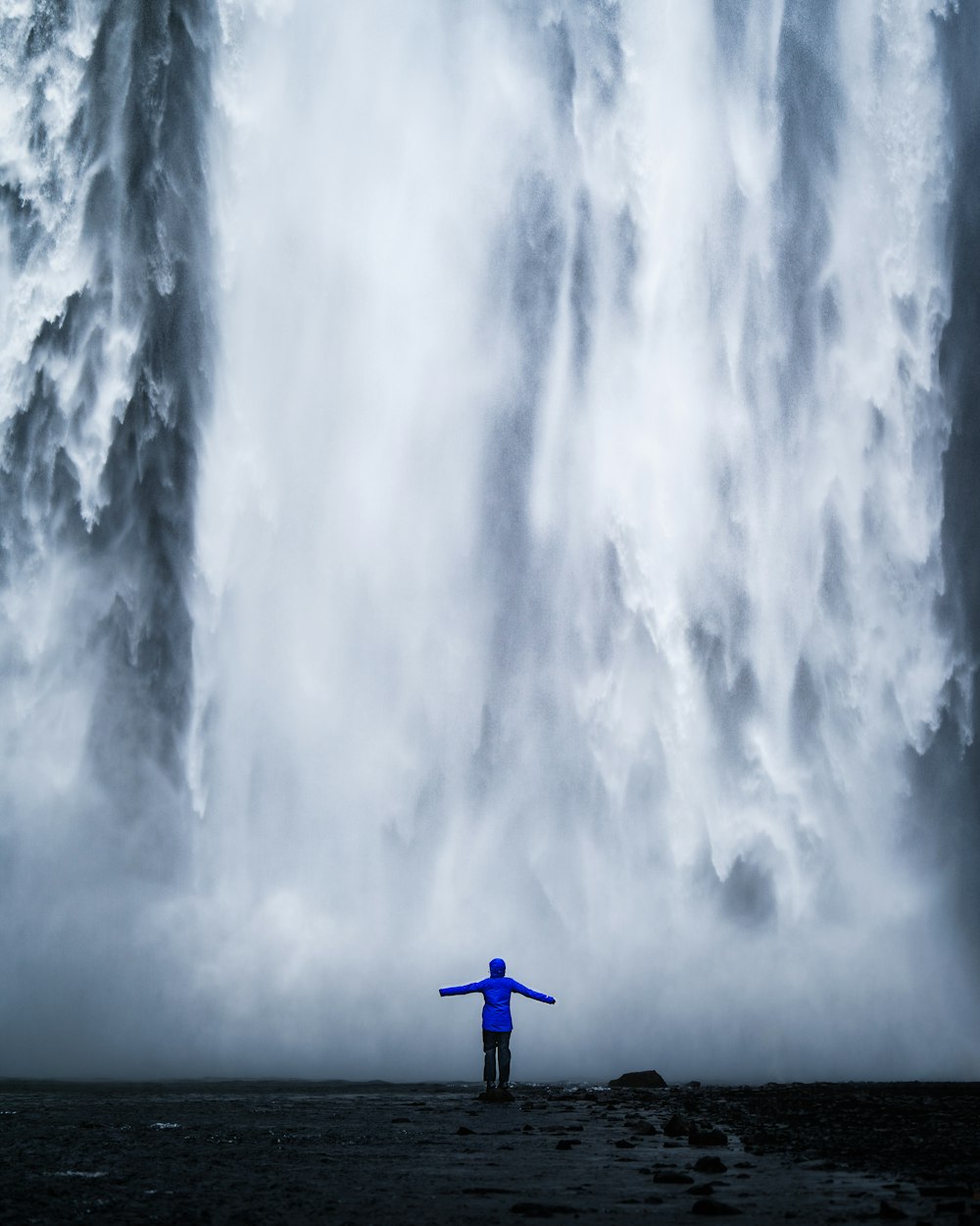 青いジャケットを着た人が滝の前に立つ