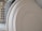 Several white plates are neatly stacked in a row, positioned vertically. In the background, a stainless steel utensil holder with circular cutouts is partially visible.