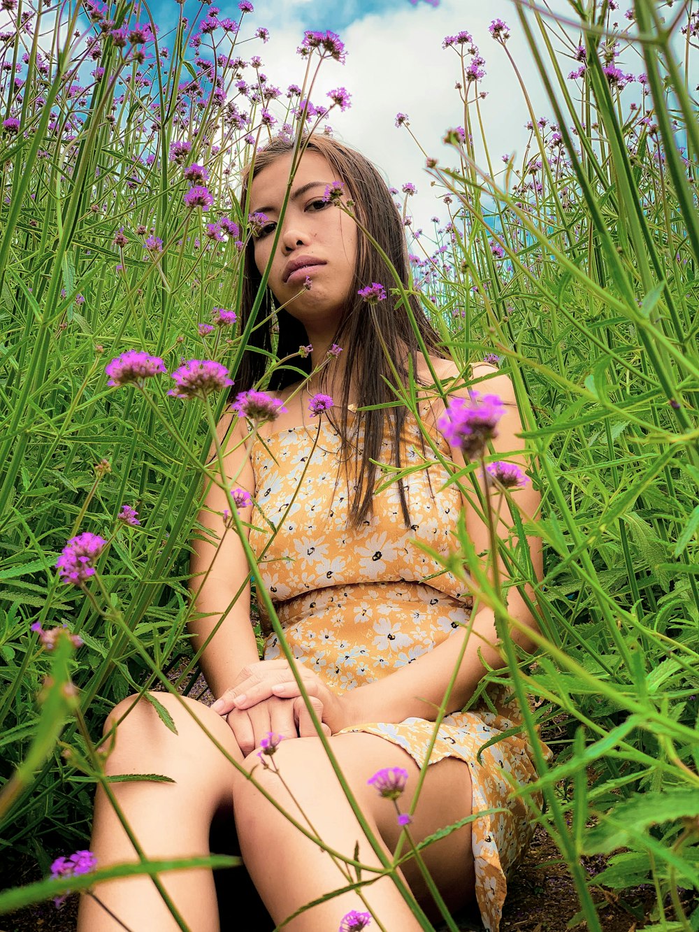 Femme assise sur le sol entourée de fleurs aux pétales violets