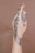 A hand adorned with intricate henna designs featuring a mix of floral and geometric patterns. The artwork extends from the fingertips, with dense details, and continues along the hand's back towards the wrist. The background is a plain, soft brown color, which helps highlight the black henna designs.