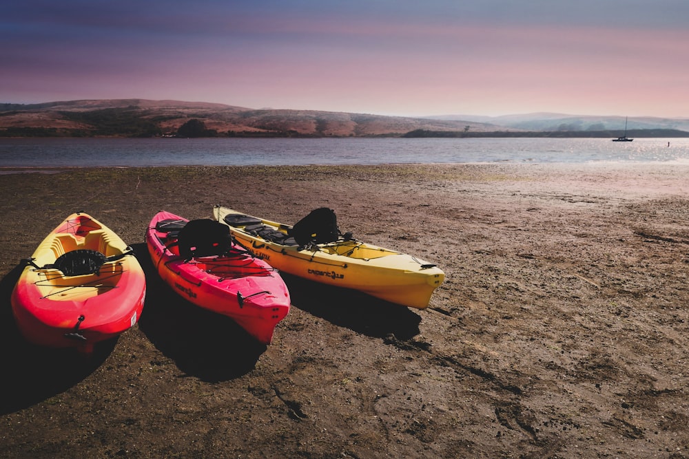 two red and one yellow kayaks near shore