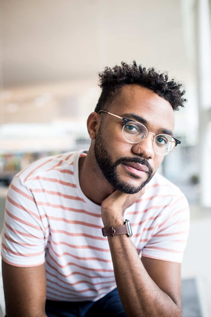 Young man with glasses and striped shirt, resting chin on hand, reflecting on workplace safety and ergonomics training.