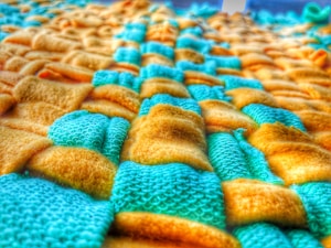 A close-up of a textured fabric with a woven pattern, featuring a combination of yellow and teal colored fibers. The fabric appears soft and plush, with a detailed view of both smooth and textured surfaces.