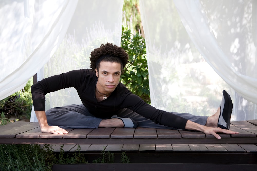 man wearing black long-sleeved Henley shirt stretching on wooden table