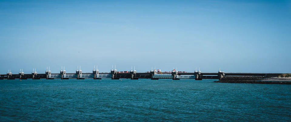 Black metal bridge spanning across water, extending into the distance beyond the horizon