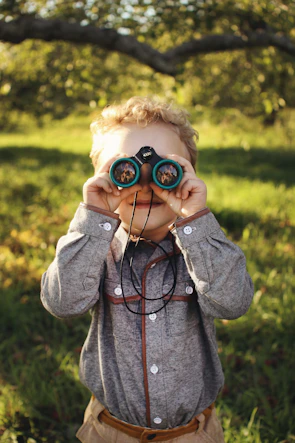 Kids learning to identify bird calls with binoculars in a lush park.