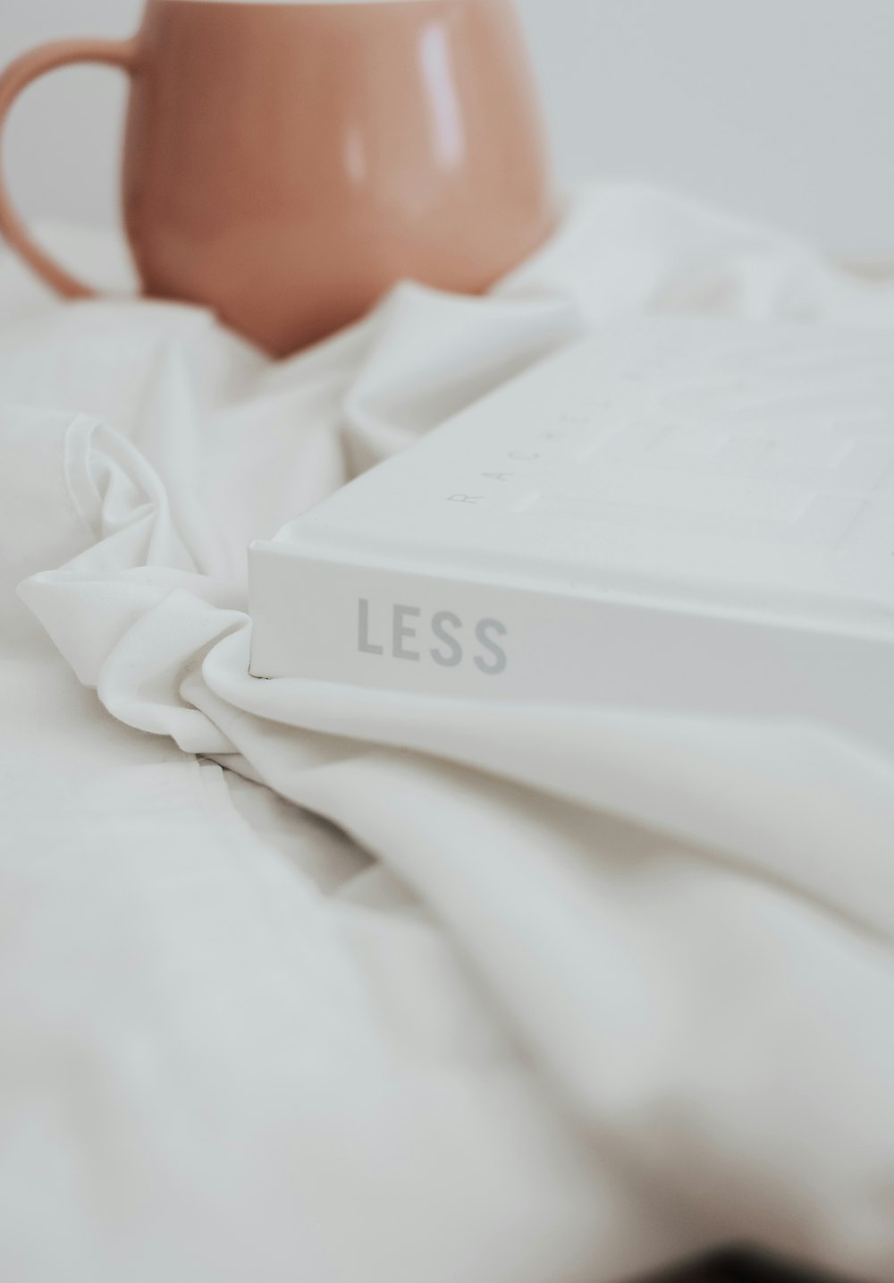 a coffee mug sitting on top of a bed next to a book