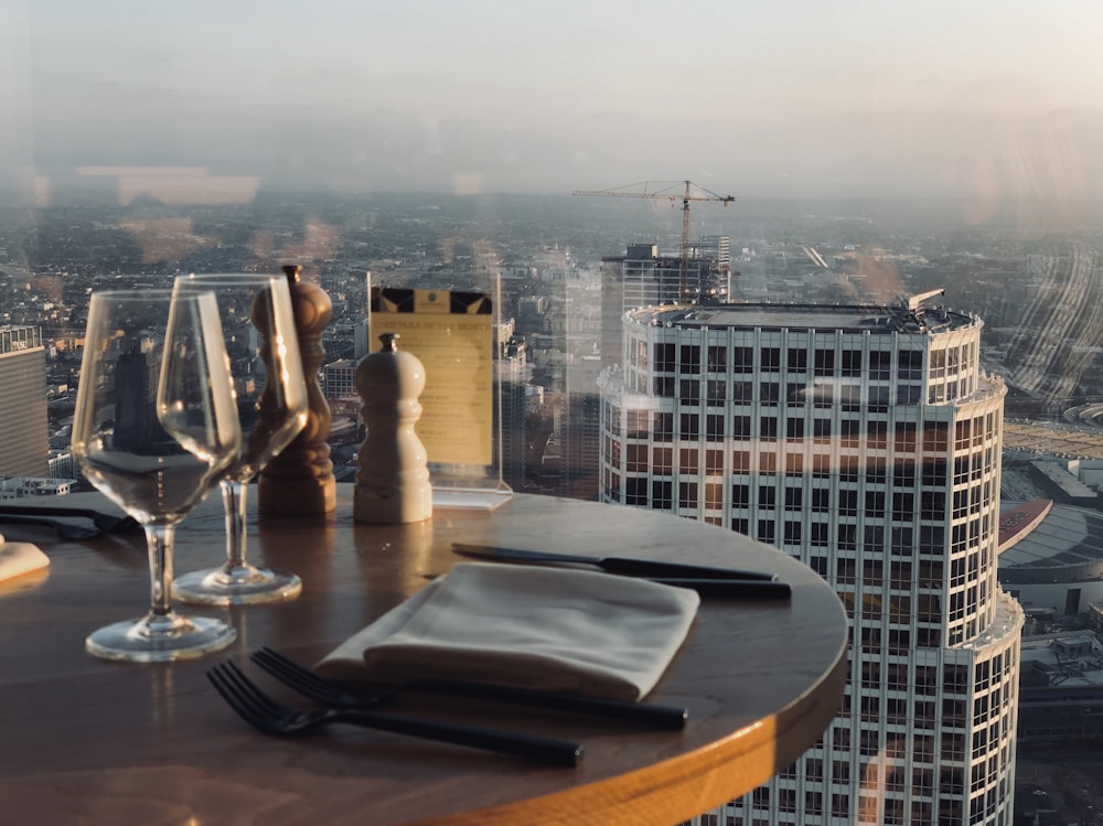 empty wineglasses beside napkin, forks, and condiment shakers on table beside glass window with city view