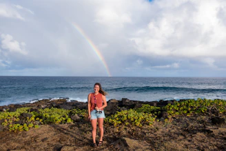woman standing in front of body of water and rainbow