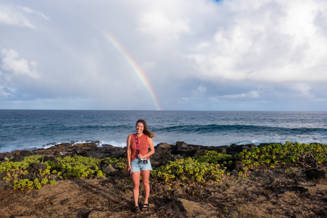 woman standing in front of body of water and rainbow