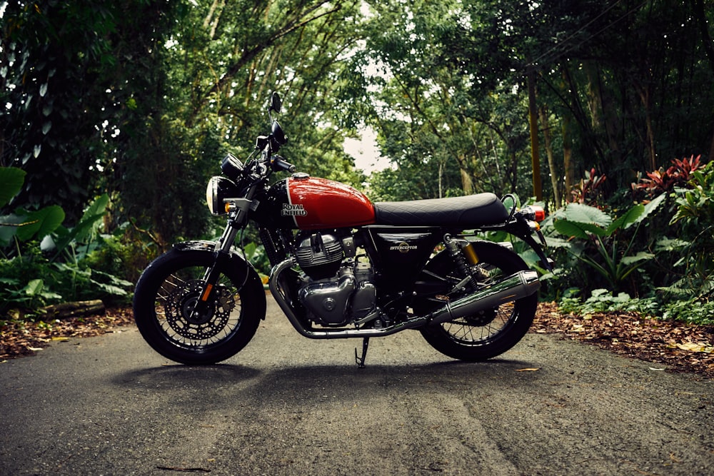 motocicleta padrão vermelha e preta no meio da estrada perto de árvores