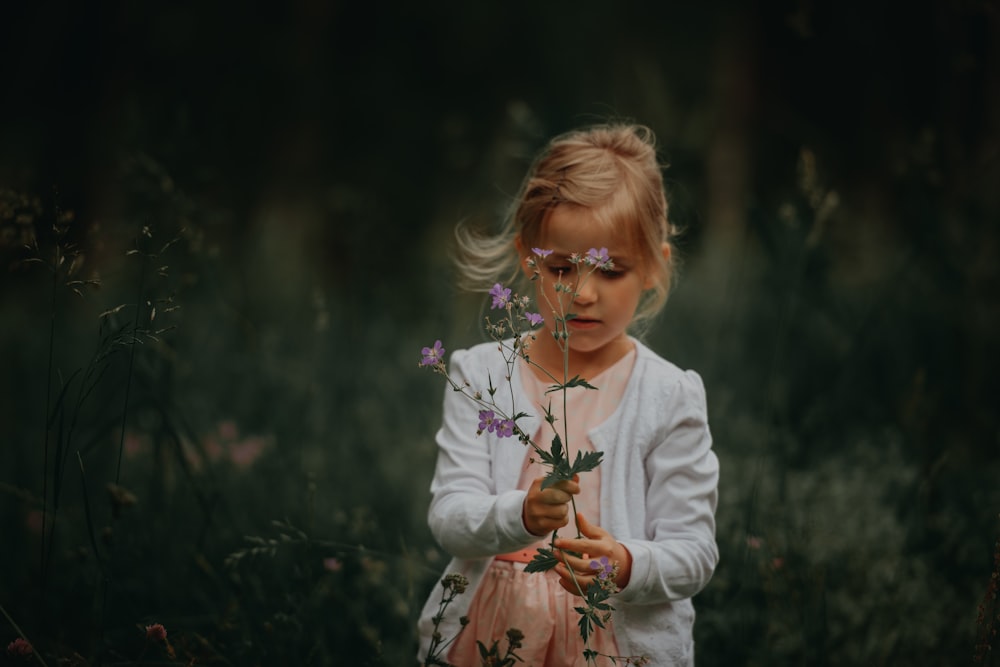 fotografia de foco seletivo da menina segurando a flor