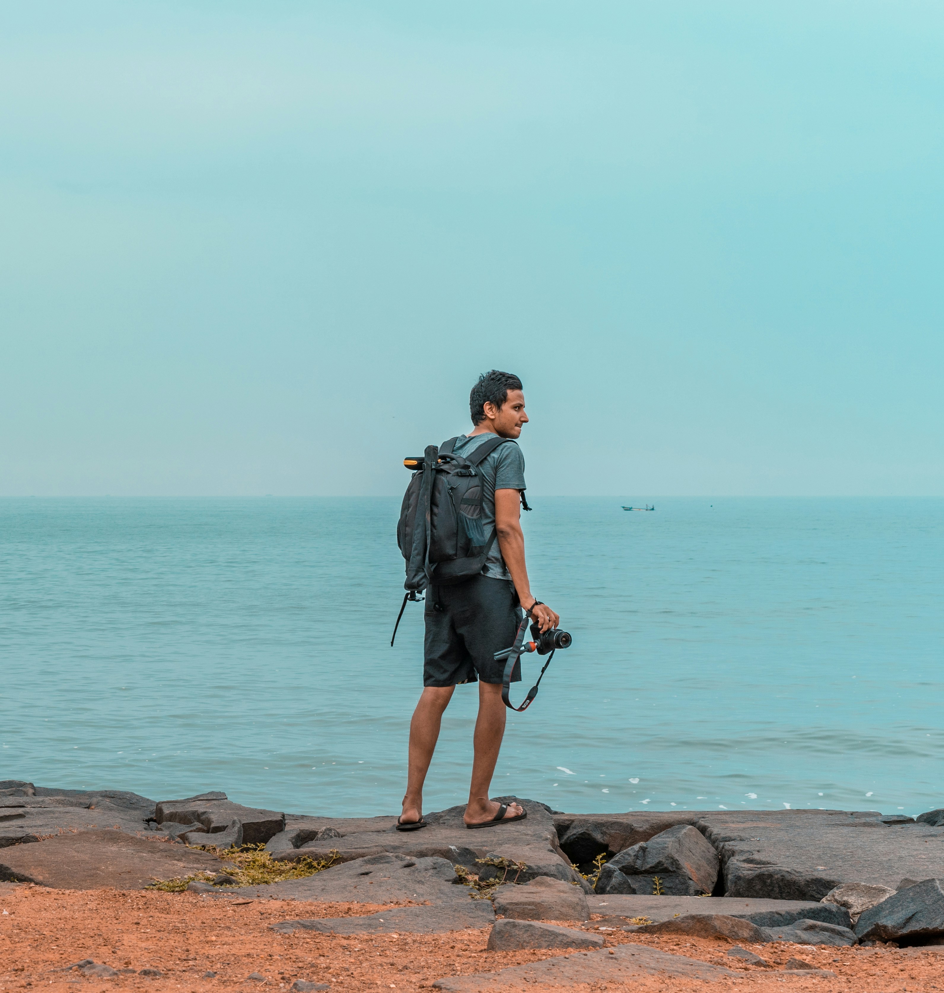 man standing on rock seashore holding camera during day
