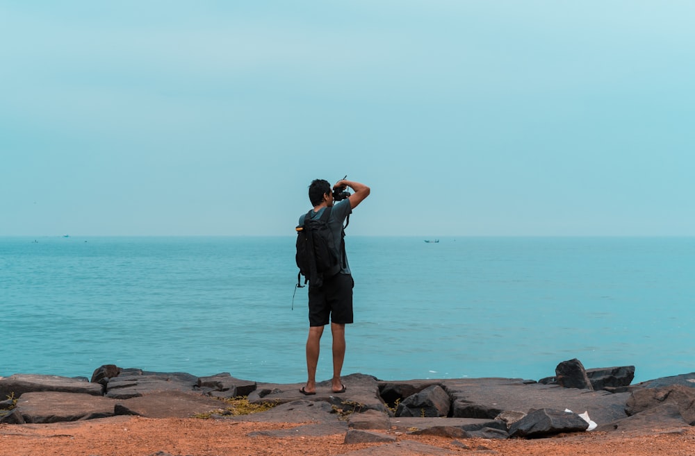 man standing on cliff using camera