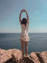 woman raising hands standing on cliff at daytime
