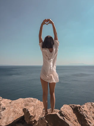 woman raising hands standing on cliff at daytime