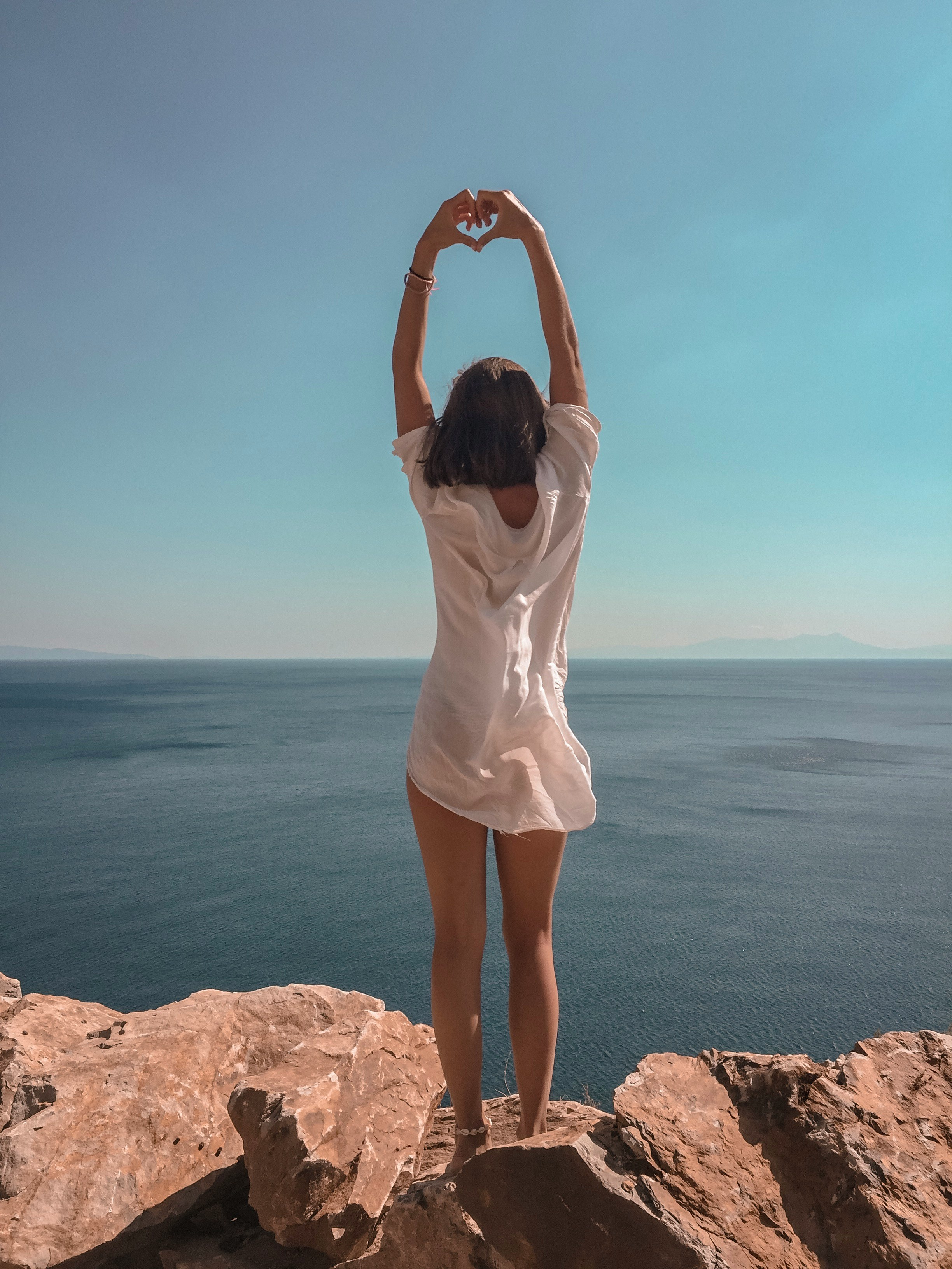 woman raising hands standing on cliff at daytime