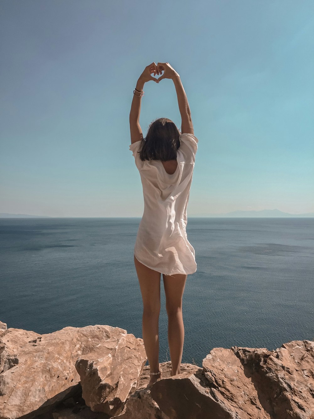 woman raising hands standing on cliff at daytime