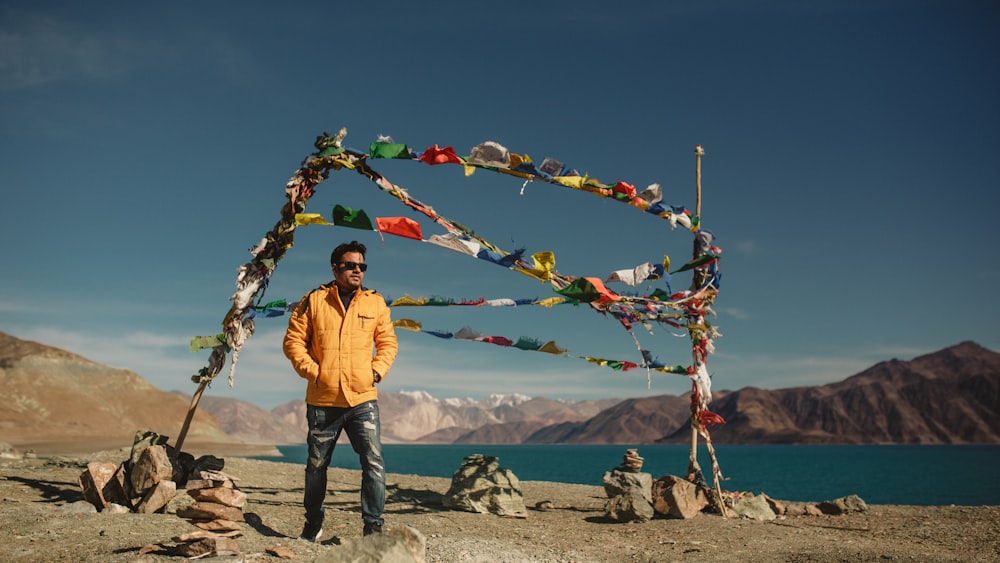 man wearing orange zip-up jacket standing near blue body of water