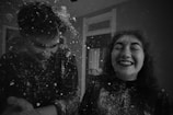 Two people are laughing joyfully as they playfully throw what appears to be flour or powder at each other. The scene is captured in black and white, adding a classic and timeless feel.