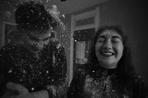 Two people are laughing joyfully as they playfully throw what appears to be flour or powder at each other. The scene is captured in black and white, adding a classic and timeless feel.