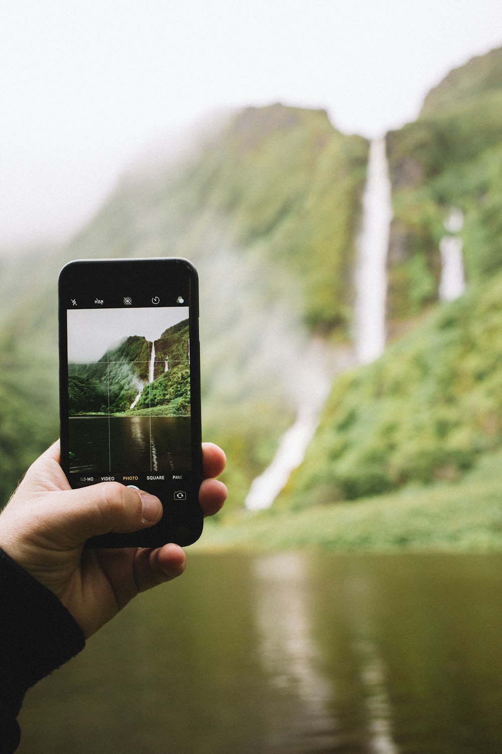 person taking photo of waterfall