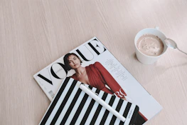 Close-up of glossy journal, coffee cup, and heels arranged on a sleek black surface with chrome and gold accents.