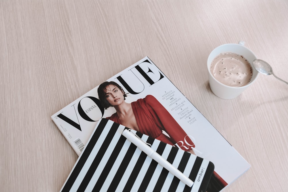 caneta branca tampada em cima da revista Vogue ao lado da xícara de café