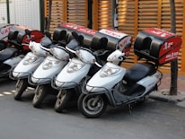 A fleet of delivery bikes lined up ready for dispatch in front of a modern warehouse.