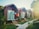 Several wooden cabins with thatched roofs are lined up along a pathway, surrounded by lush greenery. Clothes are hanging outside the cabins, suggesting a laid-back, vacation atmosphere. Sunlight filters through the trees, casting a warm glow over the scene.