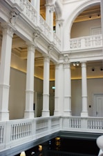 Elegant interior featuring classical architectural elements such as tall white columns, ornate moldings, and intricate railings. The space is well-lit, highlighting the detailed craftsmanship and symmetry of the design.