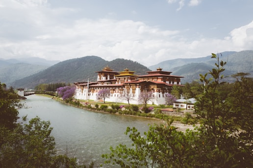 A serene Bhutanese mountain monastery nestled among lush green hills under a clear blue sky.
