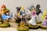 A collection of detailed and colorful figurines, primarily featuring characters in vibrant costumes. The central figure wears a blue top with a brown belt and boots, flanked by other characters in various striking outfits, all displayed on round bases.